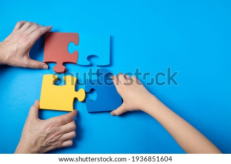 Top view hands of a autistic child and father arranging color puzzle symbol of awareness for autism spectrum disorder. Autism Awareness Day or month.
