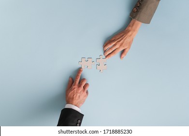 Top view of hands of businesswoman and businessman joining two blank matching puzzle pieces. Over blue background with copy space. - Shutterstock ID 1718885230