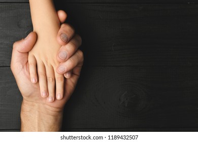 Top view, Hands of an elderly man holding the hand of a younger man. Lots of texture and character in the old man hands. on black wooden background