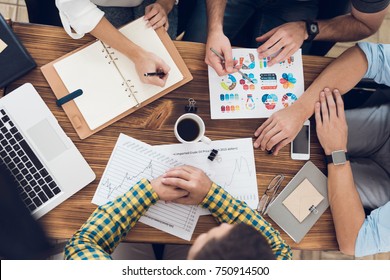 Top View Of The Hands Of The Employees Of The Business Office During The Meeting. People Are Considering Business Graphics. There Is A Cup Of Coffee On The Table, Glasses, A Smartphone And Laptop.