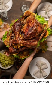 Top View Of Hands Of Female Passing Roasted Turkey To Her Husband Or Other Member Of Family Over Festive Table Served With Homemade Food