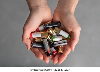 vista superior de las manos llenas de baterías alcalinas, manos de una joven caucásica, suéter blanco en el fondo, eliminación de fuentes de corriente química
