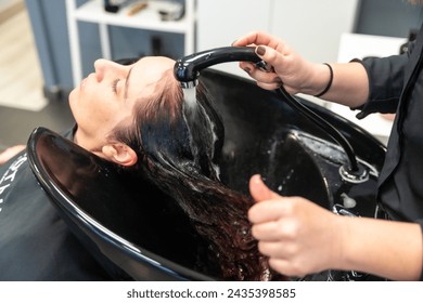 Top view of the hands of a hairdresser washing the long hair of a client in a hair salon - Powered by Shutterstock