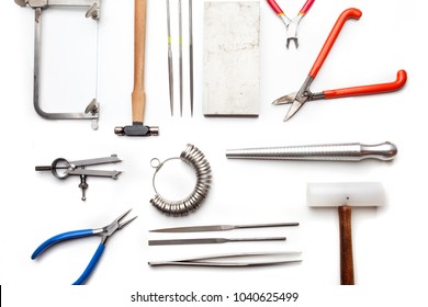 Top view of hands holding goldsmiths tools, jewelry objects. Tools over white background.