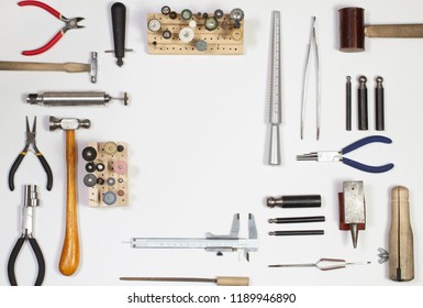 Top view of hands holding goldsmiths tools, jewelry objects. Tools over white background.