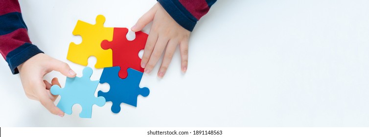 Top view hands of a little child arranging color puzzle symbol of public awareness for autism spectrum disorder. World Autism Awareness Day, ASD, Caring, Speak out, Campaign, Togetherness. Banner. - Shutterstock ID 1891148563