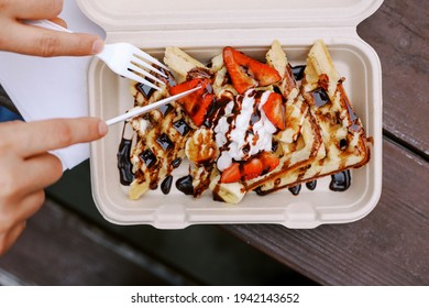 A Top View Of A Man’s Hands Using Biodegradable Utensils To Cut Into Vegan Waffles In A Compostable To-go Container On A Picnic Table