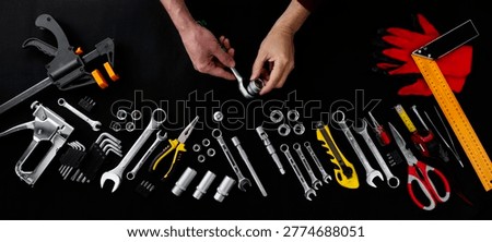 Top view of hands using a ratchet tool among a wide assortment of professional tools on a black background. Concept of repair, maintenance, construction and DIY work.