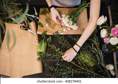Top view of hands of young woman florist creating bouquet of flowers on black table - Shutterstock ID 408278401