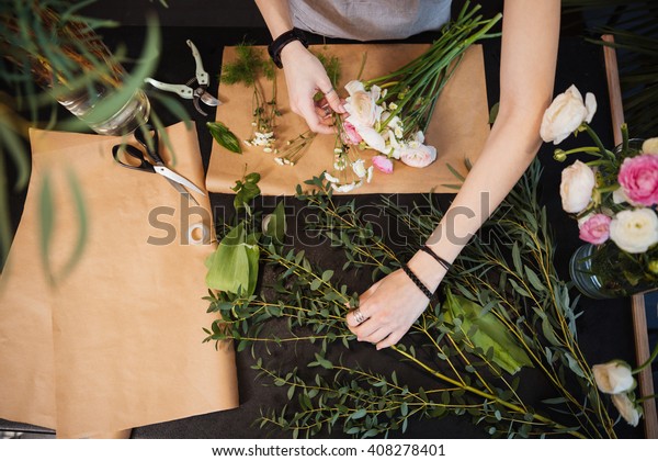 Top view of hands of young woman florist\
creating bouquet of flowers on black\
table