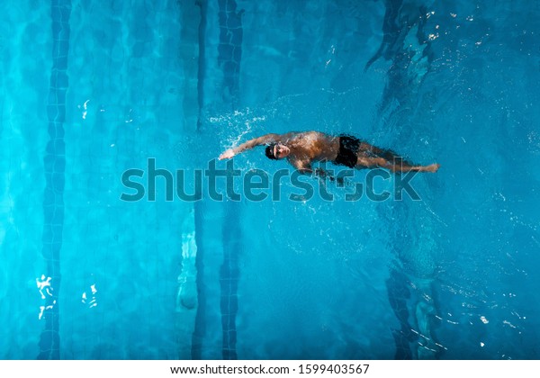 top view of handsome swimmer doing backstroke\
swimming in swimming pool