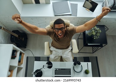 Top View Of Happy African Man Keeping Arms Raised While Sitting At His Working Place