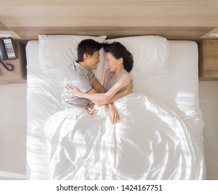 Top View Of Happy Asian Couple Smiling, And Sleeping Together On Bed In Love And Sex Concept In A Modern Bedroom With White Blanket In The Morning.