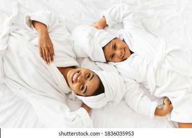 Top View Of Happy Black Mother And Daughter In Bathrobes And Towels Lying On Bed Relaxing After Spa, Pampering Themself With Beauty Treatments At Home, Mom And Child Having Fun Together, Free Space