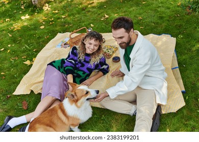 top view of happy couple cuddling cute corgi dog while having picnic on green lawn in park - Powered by Shutterstock