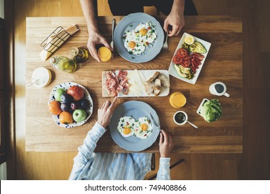 Top view of happy couple sitting at the kitchen table and having breakfast of fried eggs and vegetables - Powered by Shutterstock