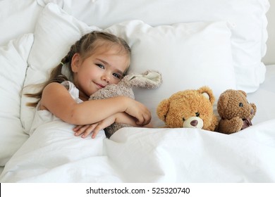 Top view of happy cute awaking girl with her toy animals, bedtime, childhood and family concept, close-up indoor portrait