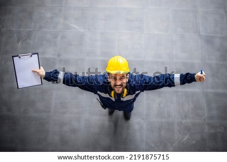 Top view of happy factory worker with raised hands celebrating promotion and success at job.