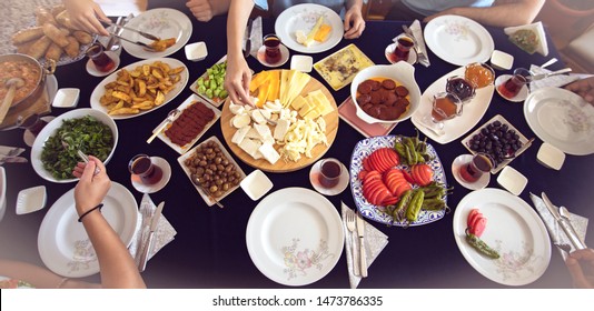 Top View Of Happy Family Having Tasty Delicious Rich Traditional Turkish Breakfast On Table In The Morning.  Flat-lay Of Peoples Hands.Bread, Ftied Eggs, Olives, Vegetables, Sausage, Cheese And Tea.