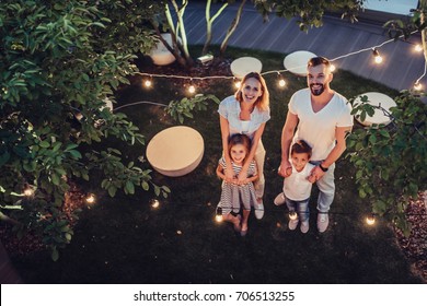 Top view of happy family is spending time together in park in the evening with garland of light bulbs. Parents with children having fun and enjoying being together. Mom, dad, son and daughter outdoors