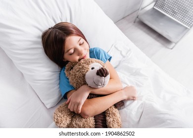 Top View Of Happy Girl Sleeping With Teddy Bear In Hospital Bed