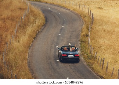 Top View. Happy Just Married Couple Is Driving A Convertible Car On A Country Road For Their Honeymoon, The Bride Have Fun With Hands Up