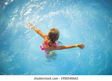 Top view happy little girl in bright color swimwear swims in the clear warm pool water Sunny summer day during vacation. Family vacation and tourism concept. Advertising space