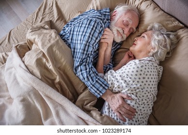 Top view of happy married woman and man lying in bed with closed eyes. They are embracing each other and smiling. Concept of love