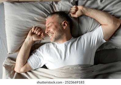 Top view of happy middle aged man enjoying happy morning, lying in bed and stretching his body after waking up, feeling well-rested - Powered by Shutterstock