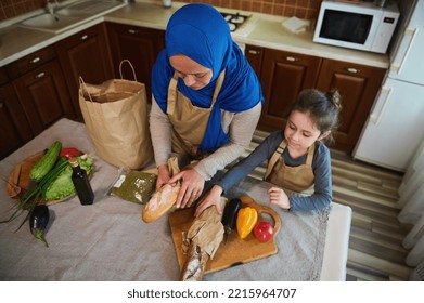 Top View. Happy Middle Eastern Family Relationship At Home. Arab Muslim Woman, Loving Mom With Little Daughter Unpacking Food, Vegetable And Fruit From Supermarket Bag Together For Preparing Meal