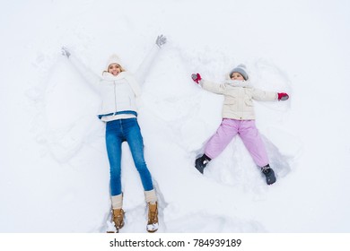 top view of happy mother and daughter making snow angels together 