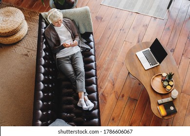 Top View Of Happy Senior Woman Enjoying Favorite Music In Headphones, Relaxing On Couch At Living Room