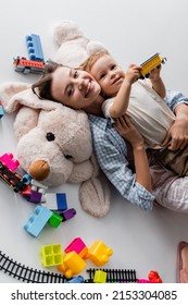 Top View Of Happy Woman Lying With Toddler Son On Toy Dog On Grey