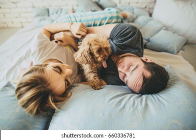 Top view of happy young family relaxing on bed together. Man and woman with pet dog in bedroom. - Powered by Shutterstock