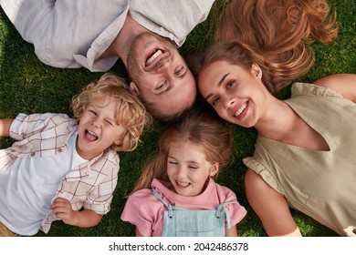 Top view of happy young parents with little daughter and son lying on green grass in summer park. Childhood, parenting, relax concept