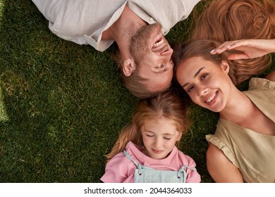 Top view of happy young parents with little daughter lying on green grass in summer park. Childhood, parenting, relax concept - Powered by Shutterstock