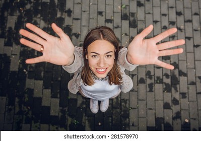 Top View Of Happy Young Trendy Woman Raising Her Hands Up Over A Gray Street Paving Stone Background