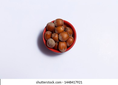 Top view of hazelnuts inside a red bowl isolated on white background.