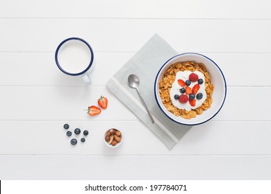 Top View Of Healthy Breakfast With Cereals, Berries, Honey And Nuts In An Enamel Bowl On A White Wood Background