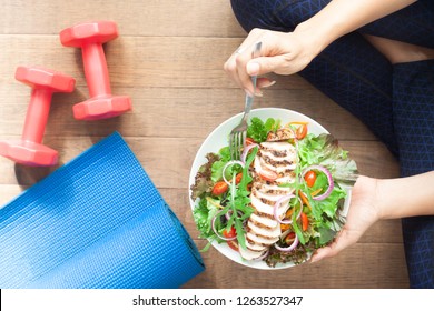 Top View Healthy Girl Eating Chicken Salad. Dumbbells And Yoga Mat On The Floor