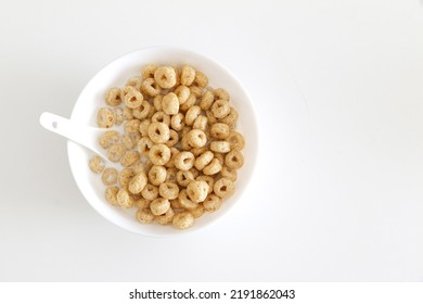 Top View Of Healthy Morning Oat Cereal, Cheerios In Bowl Of Milk With Spoon, On Left Side Of White Table Background, A Low Sugar And High Fibre Breakfast. Copy Space