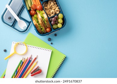 Top view of a healthy school lunchbox, notebook, and colorful pencils arranged on a blue background - Powered by Shutterstock