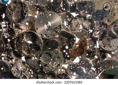 Top View Of Heap Of Metal Internal Parts Of An Old Clock On A White Light Background. Silver Clockwork With Gears And Cogwheels. Rusty Aged Vintage Watch Parts. Clock Parts In Workshop. Close Up.