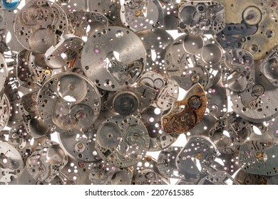 Top View Of Heap Of Metal Internal Parts Of An Old Clock On A White Light Background. Silver Clockwork With Gears And Cogwheels. Rusty Aged Vintage Watch Parts. Clock Parts In Workshop. Close Up.