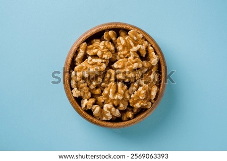 Top view of heap of walnut kernels in wooden bowl on blue background