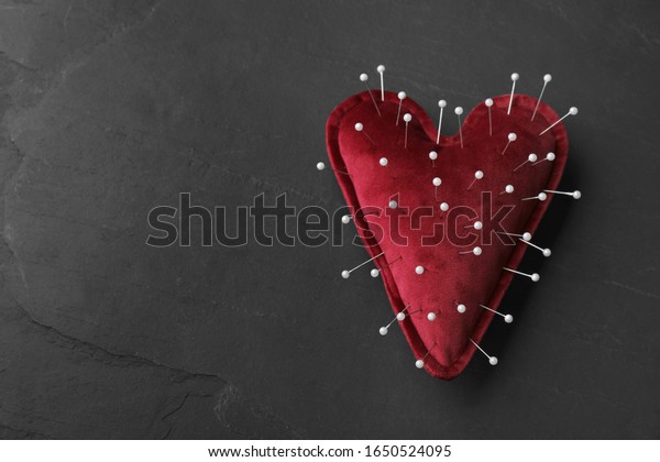 Top view of heart shaped cushion with sewing pins\
on black stone background, space for text. Relationship problems\
concept