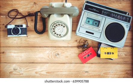 Top view hero header - retro technology of radio cassette recorder with retro tape cassette, vintage telephone and film camera on wood table. Vintage color effect styles. 