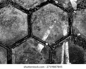 Top view of hexagonal paving blocks in high contrast black and white. Grayscale macro texture of weathered concrete stones with wild grass for industrial and architectural background.