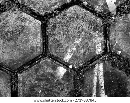 Top view of hexagonal paving blocks in high contrast black and white. Grayscale macro texture of weathered concrete stones with wild grass for industrial and architectural background.
