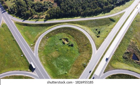 Top view of highway with intersection and roundabout in the middle of fields on a sunny day